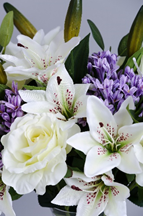 An image of an artificial flower bouquet containing white lilies and roses. 